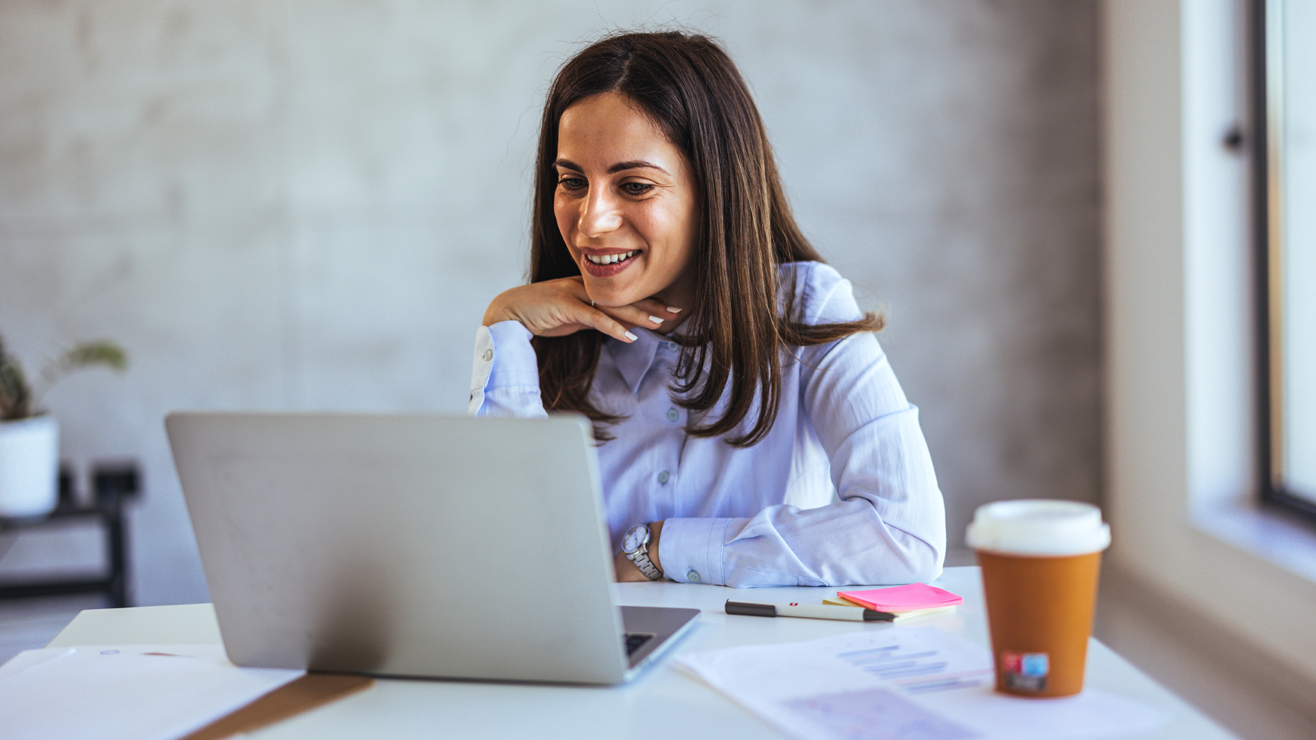 A smiling businesswoman working on her laptop while reviewing tax-related documents.