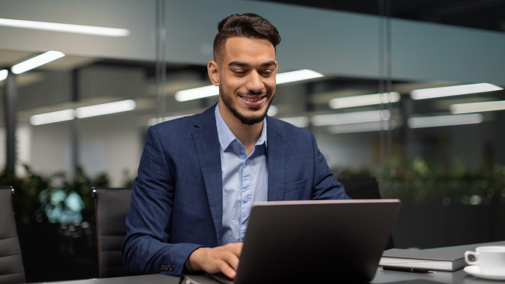 Businessman in a modern office smiling while reading tax updates on his laptop.