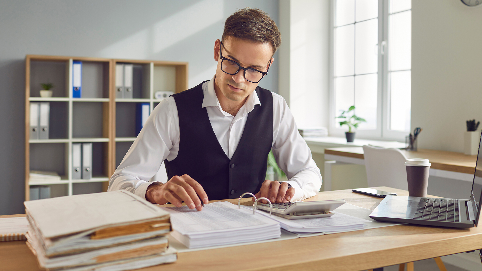 Accounting manager reviewing financial documents and calculations, analyzing reports and ensuring accuracy in financial records.