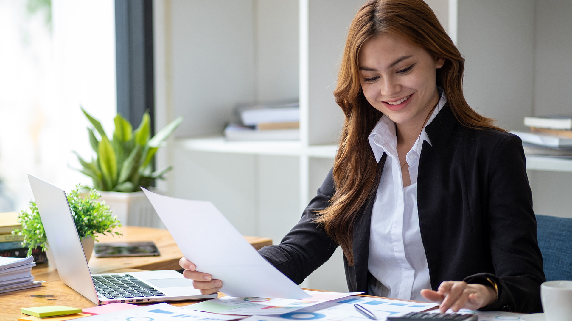 Business professional reviewing financial reports and calculating data at a desk, representing accounting and financial analysis tasks.
